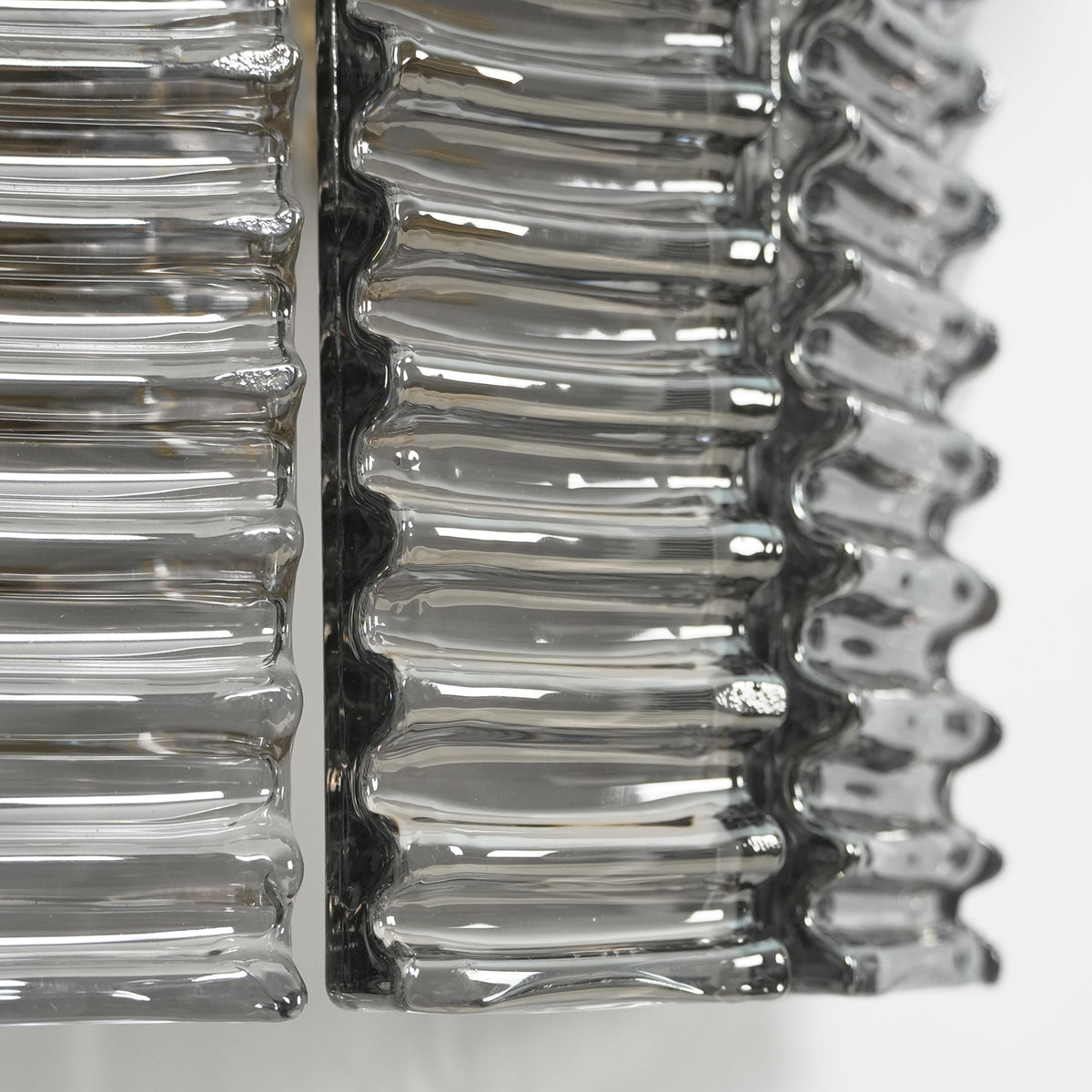 Vespera Tiered Smoky Glass Wall Lamp | Glass, Metal | Extreme macro focus on the undulating wavy edge texture of the glossy clear smoky glass rods under studio light | Detail shot | Severn Lighting