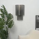 Vespera Tiered Smoky Glass Wall Lamp | Glass, Metal | Showcasing the unlit translucent smoky grey glass design on a plain white wall next to a large tropical green plant | Severn Lighting