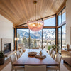 A pink chandelier of faceted rose glass hanging over a long wood dining table with mountain views.