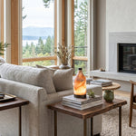 Aldric Alabaster Flask Table Lamp | Natural Alabaster Stone and Bronze Metal | Casting a warm ambient glow on a side table next to a cream sofa in a coastal or lakefront living room | Severn Lighting
