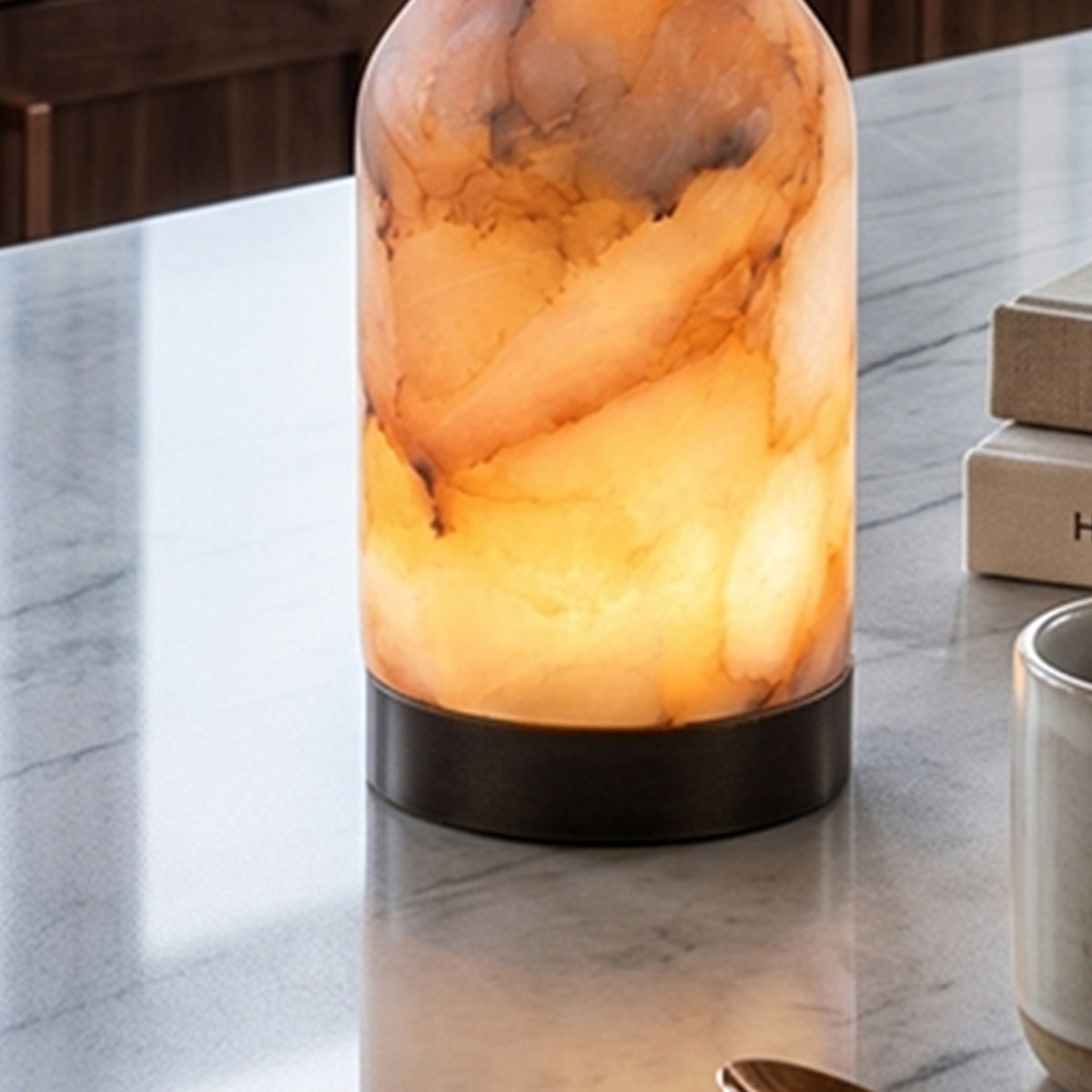 Aldric Alabaster Flask Table Lamp | Natural Alabaster Stone and Bronze Metal | Detailed reflection view of the warm amber stone body glowing on a polished marble surface | Severn Lighting
