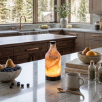 Aldric Alabaster Flask Table Lamp | Natural Alabaster Stone and Bronze Metal | Placed on a white marble kitchen island counter next to fruit bowls and a coffee mug | Severn Lighting