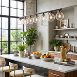 Alistair Linear Glass Globe Chandelier | Kitchen Island Lighting | Hanging elegantly in a modern industrial kitchen space, casting a warm glow over a marble countertop and wooden barstools | Severn Lighting
