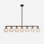 Alistair Linear Glass Globe Chandelier | Clear Glass, Brass, Metal | Isolated lit view of a modern industrial 8-light linear suspension chandelier with clear glass globes, gold brass sockets, and a sleek matte black bar | White background | Severn Lighting
