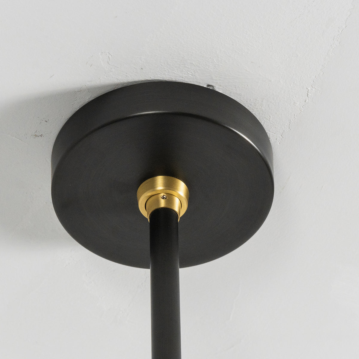 Alistair Linear Glass Globe Chandelier | Ceiling Canopy Detail | Close-up architectural view of the round matte black metal ceiling canopy with a contrasting brushed gold brass rod connector | Detail shot | Severn Lighting