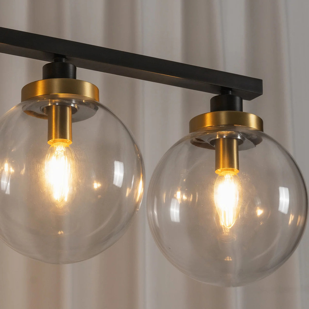 Alistair Linear Glass Globe Chandelier | Lit Bulb Detail | Macro close-up shot of the fully lit spherical clear glass globes showcasing the warm glowing bulb filaments and gold brass hardware | Detail shot | Severn Lighting