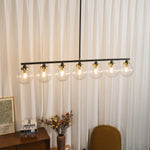 Alistair Linear Glass Globe Chandelier | Linear Island Light | Suspended gracefully against a backdrop of floor-to-ceiling white curtains above a rustic wooden console table | Severn Lighting