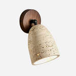 Aria Travertine Wood Wall Lamp | Travertine, Wood, Metal | Bell-shaped natural porous beige travertine shade with a round dark wood backplate and a black swivel joint | Isolated lit product shot on white background | Samu Lamp