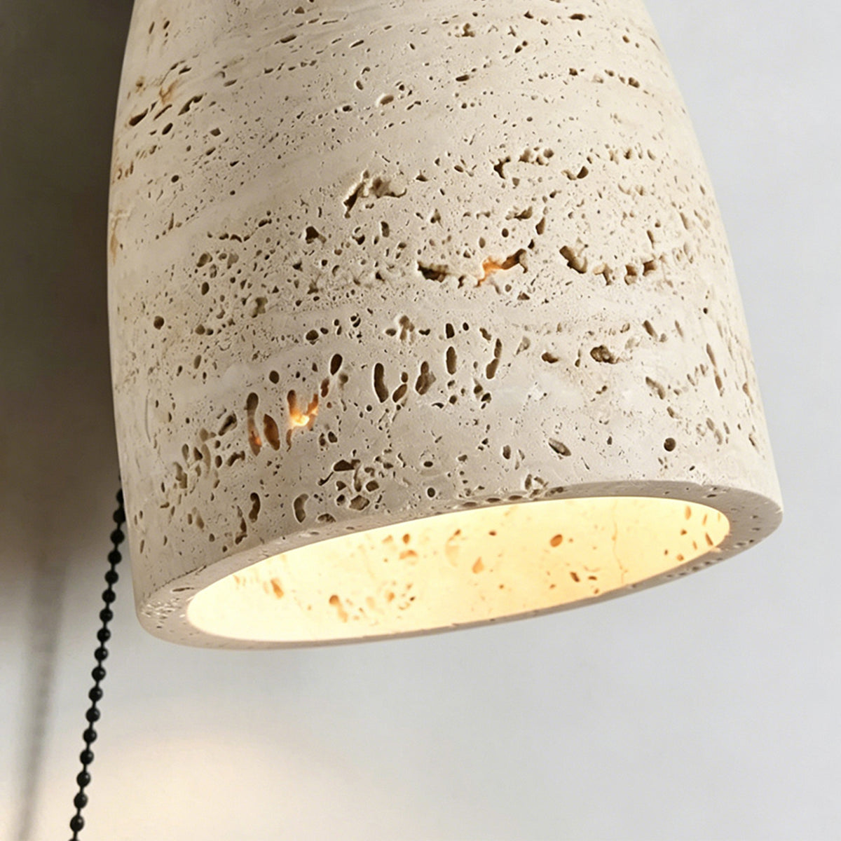 Aria Travertine Wood Wall Lamp | Travertine, Wood, Metal | Macro close-up focus on the illuminated porous travertine stone shade highlighting its natural pitted texture | Detail shot | Samu Lamp