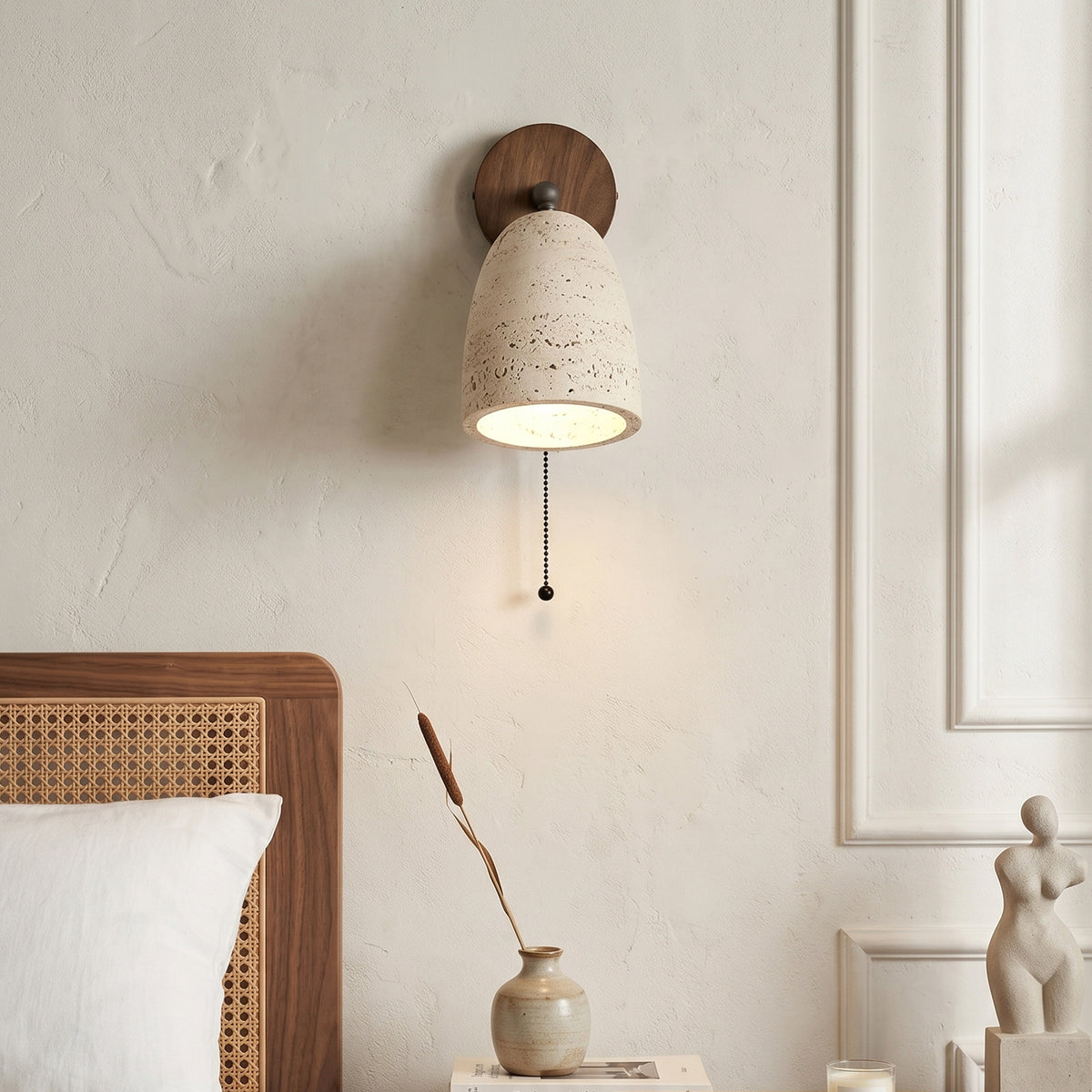 Aria Travertine Wood Wall Lamp | Travertine, Wood, Metal | Bedside view showcasing the hanging pull chain switch and cozy warm downlight over a white pillow setup | Samu Lamp