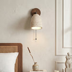 Aria Travertine Wood Wall Lamp | Travertine, Wood, Metal | Bedside view showcasing the hanging pull chain switch and cozy warm downlight over a white pillow setup | Samu Lamp