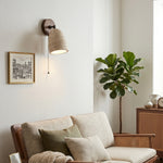 Aria Travertine Wood Wall Lamp | Travertine, Wood, Metal | Providing warm ambient light above a cream fabric sofa next to a fiddle-leaf fig tree in a modern living room | Samu Lamp