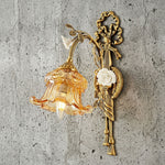 Armelle Rose Glass Brass Wall Lamp | Glass, Ceramic and Brass | Angled view glowing warmly against a textured stone backdrop | Severn Lighting