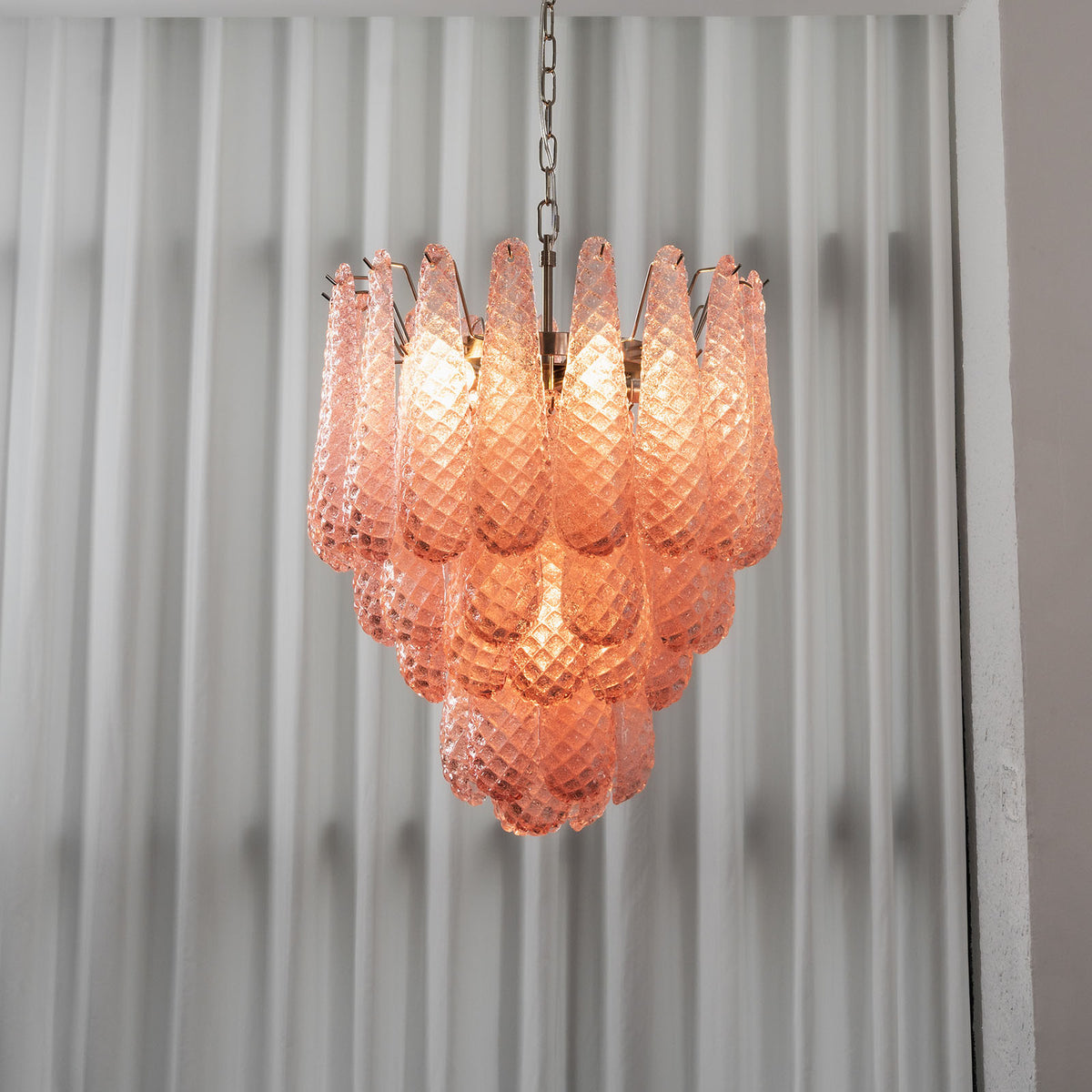 Aubine Pink Textured Glass Tiered Chandelier | Pink Textured Glass and Brass | Real-life view glowing softly against sheer white window drapes | Severn Lighting