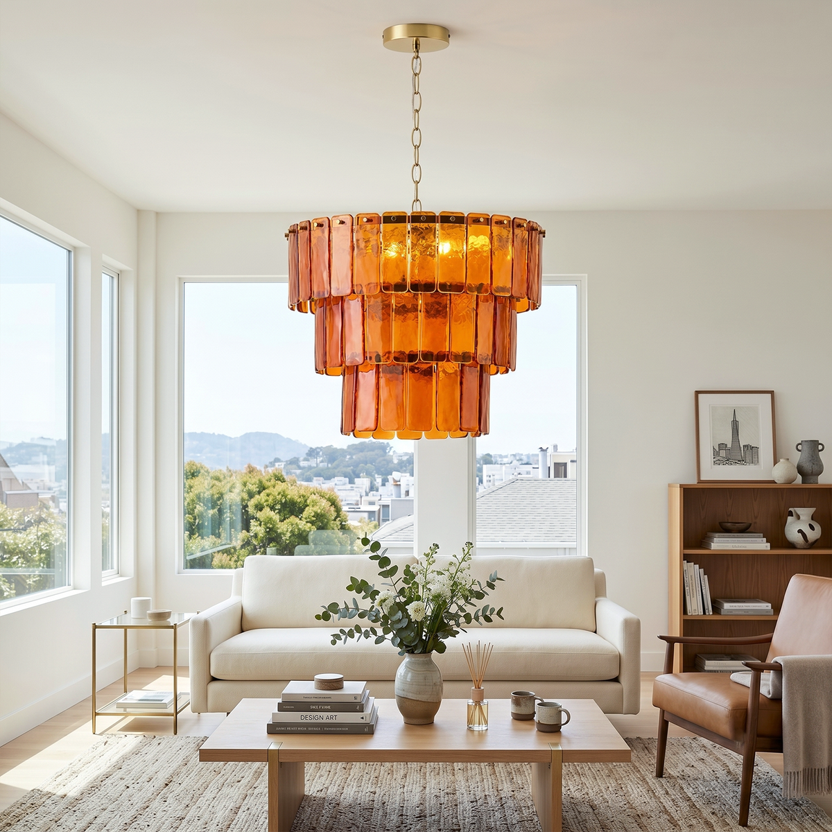 Aurelia Tiered Amber Glass Chandelier | Glass, Metal | Providing a warm golden glow in a bright minimalist living room setup with a white couch and potted indoor trees | Severn Lighting