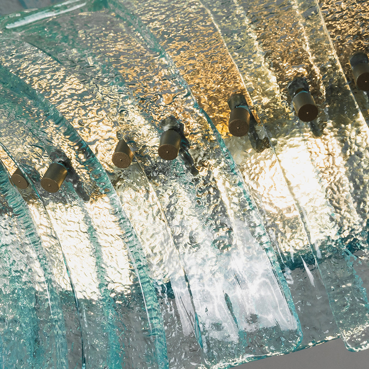 Azura Aquamarine Cascading Glass Chandelier | Glass, Metal | Low angle shot looking up at the illuminated textured glass blocks diffusing a warm golden light through the blue-green panels | Detail shot | Severn Lighting