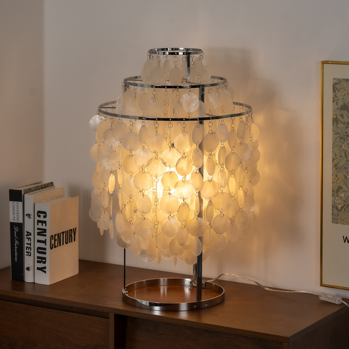 Callista Tiered Capiz Table Lamp | Capiz, Metal | Placed on a dark wood credenza console next to stacked books, creating a cozy light halo against a clean white wall | Severn Lighting