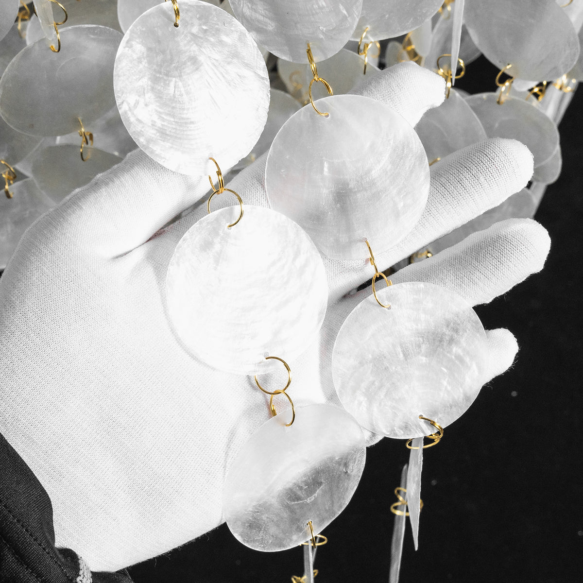 Callista Tiered Capiz Table Lamp | Capiz, Metal | Detail shot showing a white-gloved hand gently cradling the individual cascading white translucent capiz shell discs | Detail shot | Severn Lighting