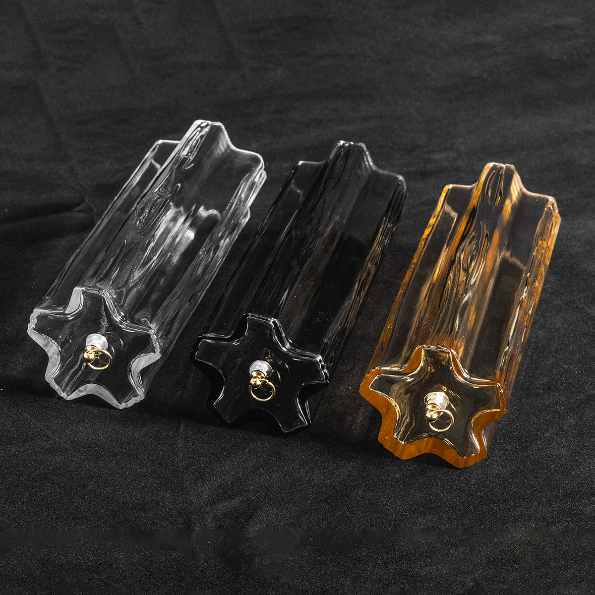 Cassian Tiered Fluted Glass Ceiling Light | Tiered Fluted Glass and Gold Brass | Detailed shot of three individual clear, smoked, and amber star-shaped glass prisms lying side by side | Severn Lighting