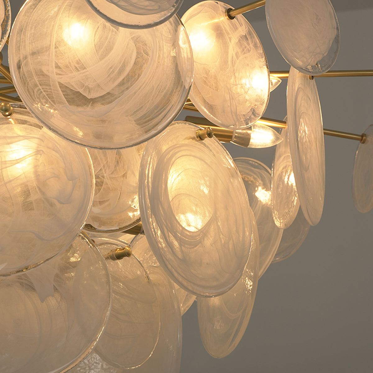 Celestia Art Glass Disc Chandelier | Glass, Metal | Macro close-up view of overlapping lit textured glass discs emitting a cozy golden ambient light halo | Detail shot | Severn Lighting