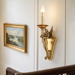 Clemency Winged Figure Brass Sconce | Cast Brass and Glass | Medium shot glowing beside a framed landscape painting near stairs | Severn Lighting