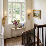 Clemency Winged Figure Brass Sconce | Cast Brass and Glass | Mounted on a hallway wall near a wooden staircase and console table | Severn Lighting