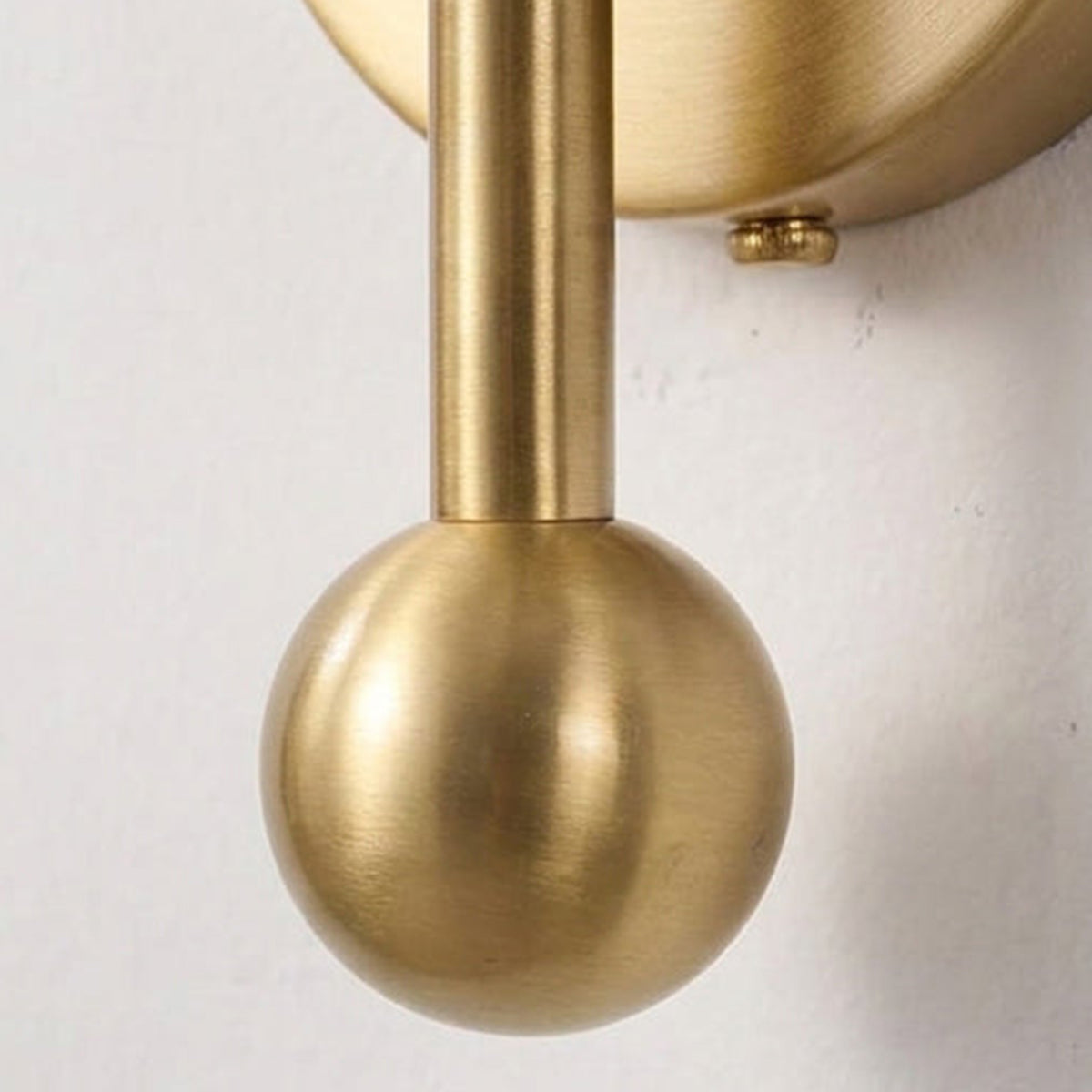 Cordelia Alabaster Globe Wall Sconce | Natural Alabaster and Brushed Brass | Extreme macro close-up focusing on the polished gold sphere finial at the bottom of the stem | Severn Lighting