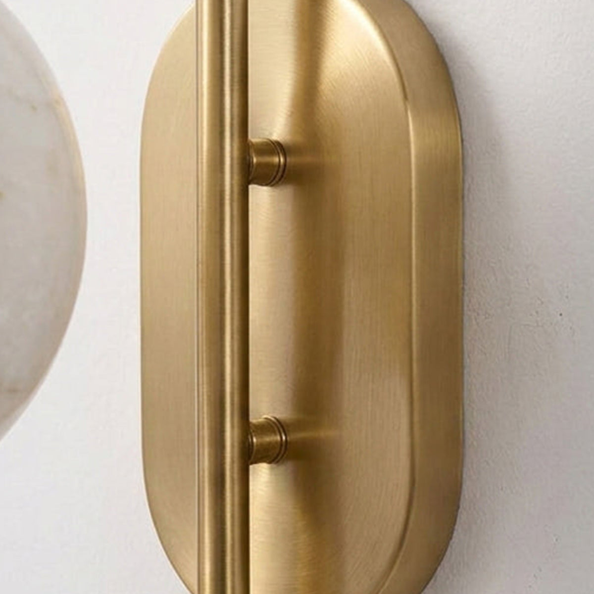 Cordelia Alabaster Globe Wall Sconce | Natural Alabaster and Brushed Brass | Detailed close-up view highlighting the smooth oval metal backplate and mounting hardware | Severn Lighting