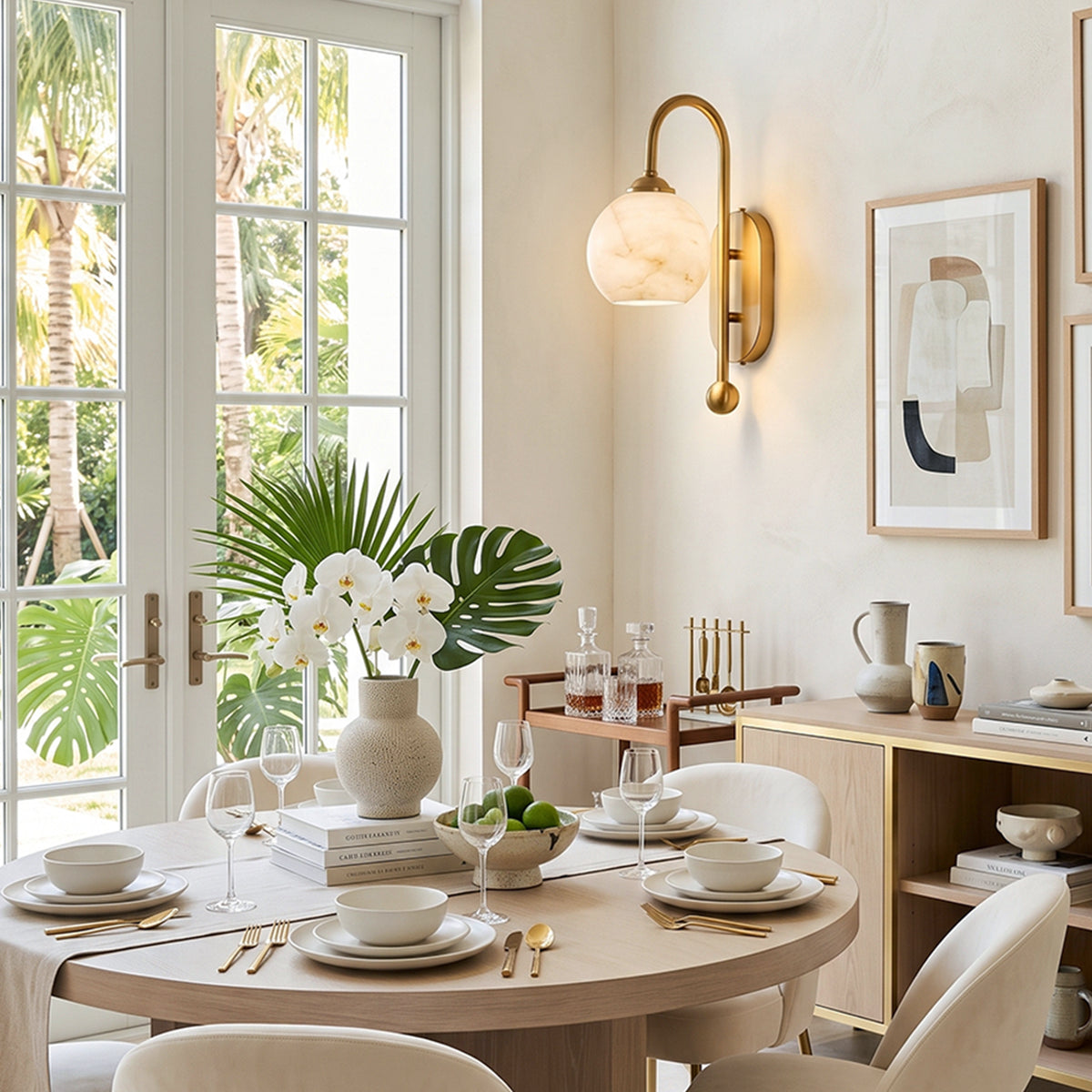 Cordelia Alabaster Globe Wall Sconce | Natural Alabaster and Brushed Brass | Casting a warm glow in a bright dining room above a round wooden table with white flowers | Severn Lighting