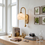 Cordelia Alabaster Globe Wall Sconce | Natural Alabaster and Brushed Brass | Mounted on a wall over a wooden home office desk with books and frames by a window | Severn Lighting