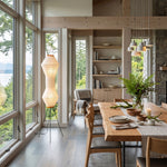 Cosima Hourglass Washi Paper Floor Lamp | Japanese Wabi-Sabi Paper and Black Tripod | Casting a warm ambient glow in a bright open-concept dining area with large glass walls | Severn Lighting