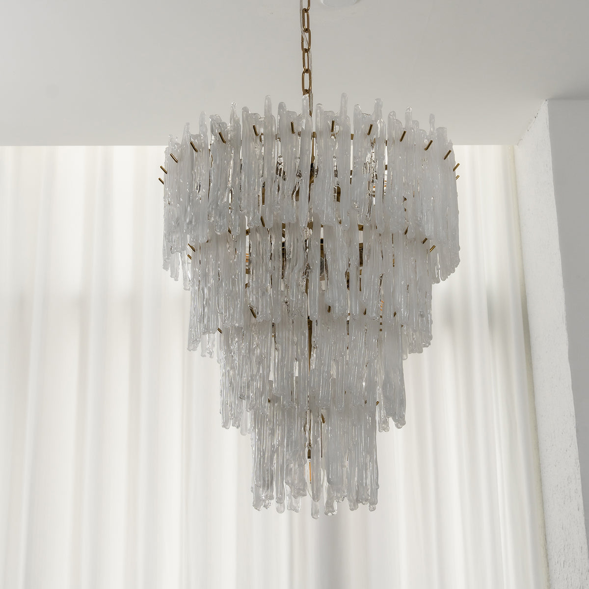 Ethereal Icicle Waterfall Chandelier | Frosted Icicle Glass and Gold Brass | Unlit standard product display hanging against white sheer backdrop curtains | Severn Lighting