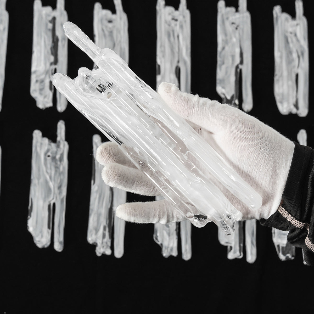 Ethereal Icicle Waterfall Chandelier | Frosted Icicle Glass and Gold Brass | A gloved hand holding a bundle of unlit textured white icicle glass rod components over a dark surface | Severn Lighting