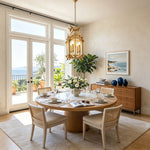 Florian Fretwork Brass Lantern Pendant Light | Glass and Brass | Suspended over a round wooden dining table in a room with sea views | Severn Lighting
