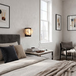 Freya Angular Alabaster Wall Sconce | Minimalist Bedroom | Positioned as a sleek bedroom wall light fixture casting a cozy golden halo near a bed with dark grey cushions | Severn Lighting