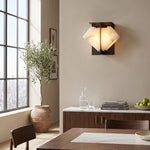 Freya Angular Alabaster Wall Sconce | Dining Room Ambient Light | Fully lit geometric stone sconce casting a warm yellow halo on a beige wall near a wooden dining setup | Severn Lighting