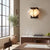 Freya Angular Alabaster Wall Sconce | Dining Room Ambient Light | Fully lit geometric stone sconce casting a warm yellow halo on a beige wall near a wooden dining setup | Severn Lighting