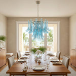 Isar Blue Petal Glass Chandelier | Blue Glass and Brass | Illuminating a long dining table with blue chairs facing coastal views | Severn Lighting