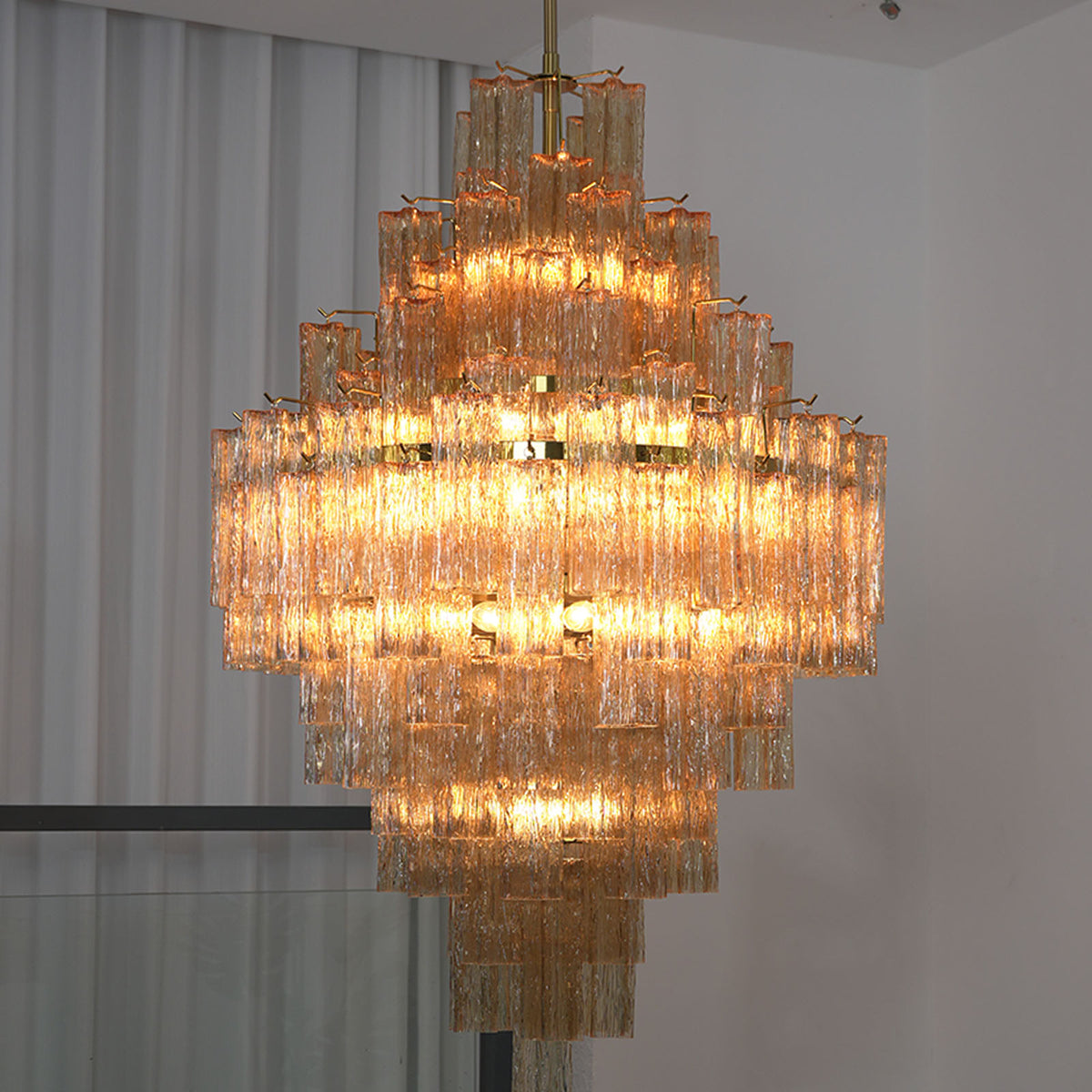 Kester Amber Glass Tier Chandelier | Amber Glass and Brass | Vertical full view of the chandelier glowing brightly in an interior space | Severn Lighting