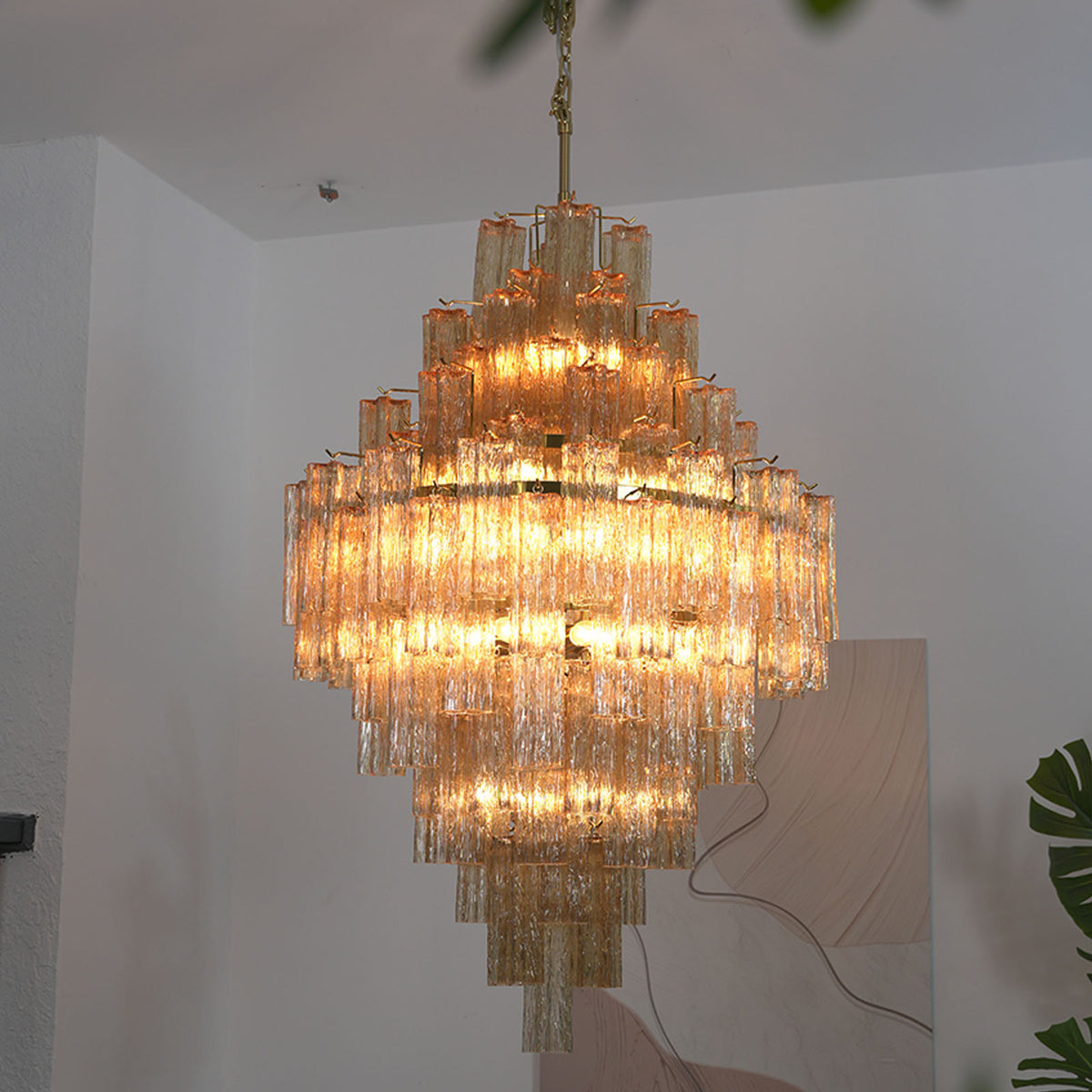 Kester Amber Glass Tier Chandelier | Amber Glass and Brass | Real-life hanging view illuminated softly against a neutral wall | Severn Lighting