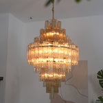 Kester Amber Glass Tier Chandelier | Amber Glass and Brass | Real-life hanging view illuminated softly against a neutral wall | Severn Lighting