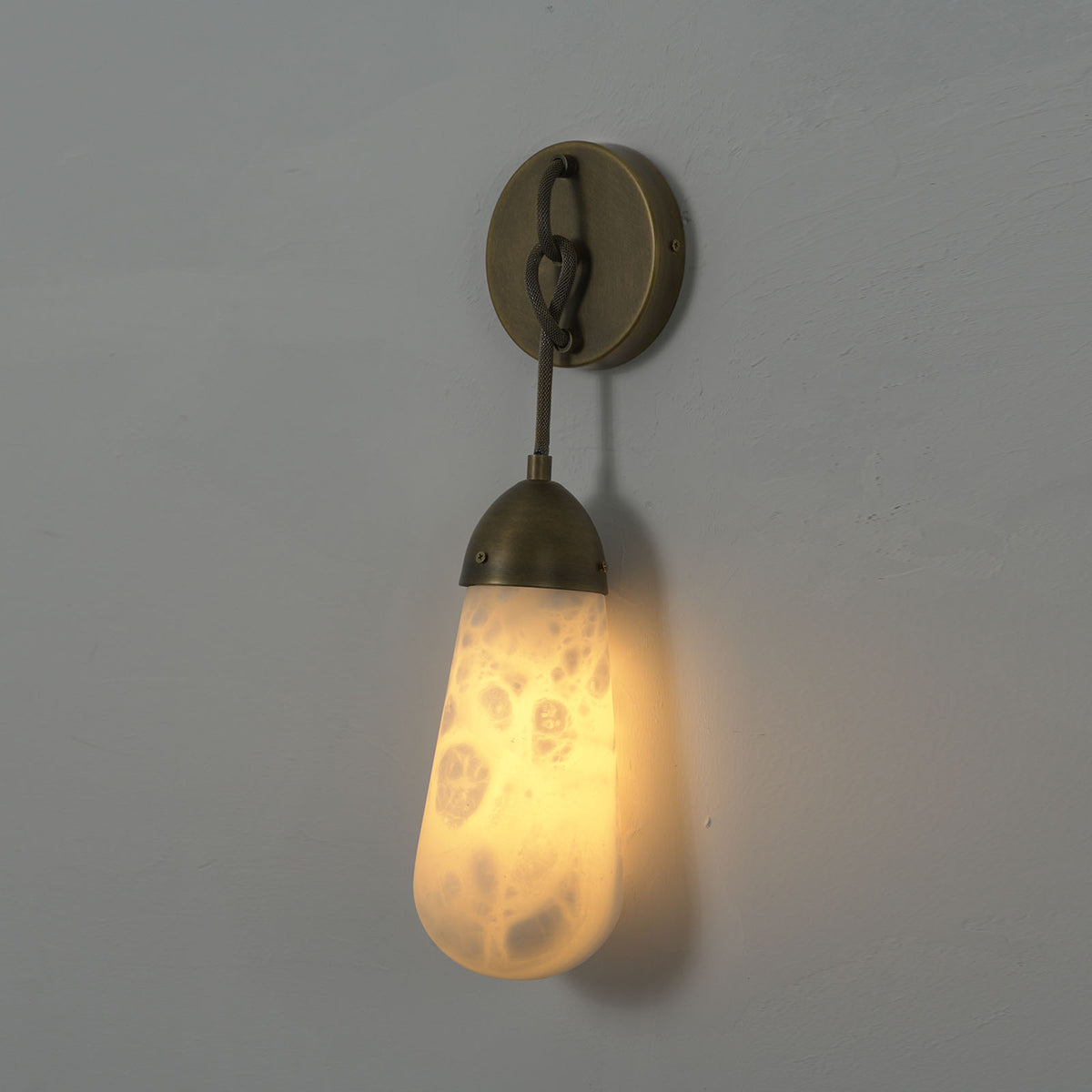 Larmelle Teardrop Sconce | Alabaster and Brass | Full illuminated view on dark wall with warm glow | Severn Lighting