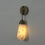 Larmelle Teardrop Sconce | Alabaster and Brass | Full illuminated view on dark wall with warm glow | Severn Lighting