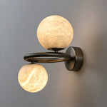 Lucern Twin Globe Alabaster Wall Sconce | Natural Alabaster and Matte Black Metal | Placed on a dark charcoal wall showcasing the warm contrast of the lit stone globes | Severn Lighting