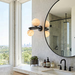 Lucern Twin Globe Alabaster Wall Sconce | Natural Alabaster and Matte Black Metal | Mounted next to a round mirror on a luxury bathroom vanity counter by a window | Severn Lighting