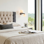 Lucern Twin Globe Alabaster Wall Sconce | Natural Alabaster and Matte Black Metal | Fixed onto a light textured bedroom wall next to a beige headboard and cozy bedding | Severn Lighting