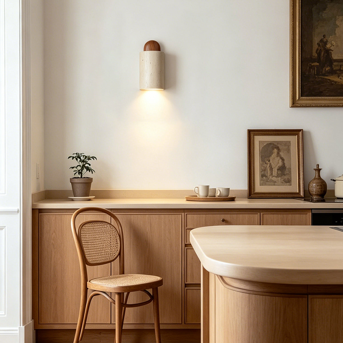 Lyra Travertine Shield Wall Lamp | Travertine, Wood, Metal | Wall-mounted sconce casting a warm downward glow over warm wood kitchen cabinetry and a classic wooden dining chair | Severn Lighting