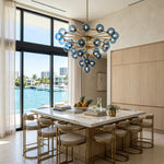 Marisol Aquamarine Glass Bubble Chandelier | Aquamarine Glass and Brass | Displayed above a kitchen dining island with floor-to-ceiling ocean view windows | Severn Lighting