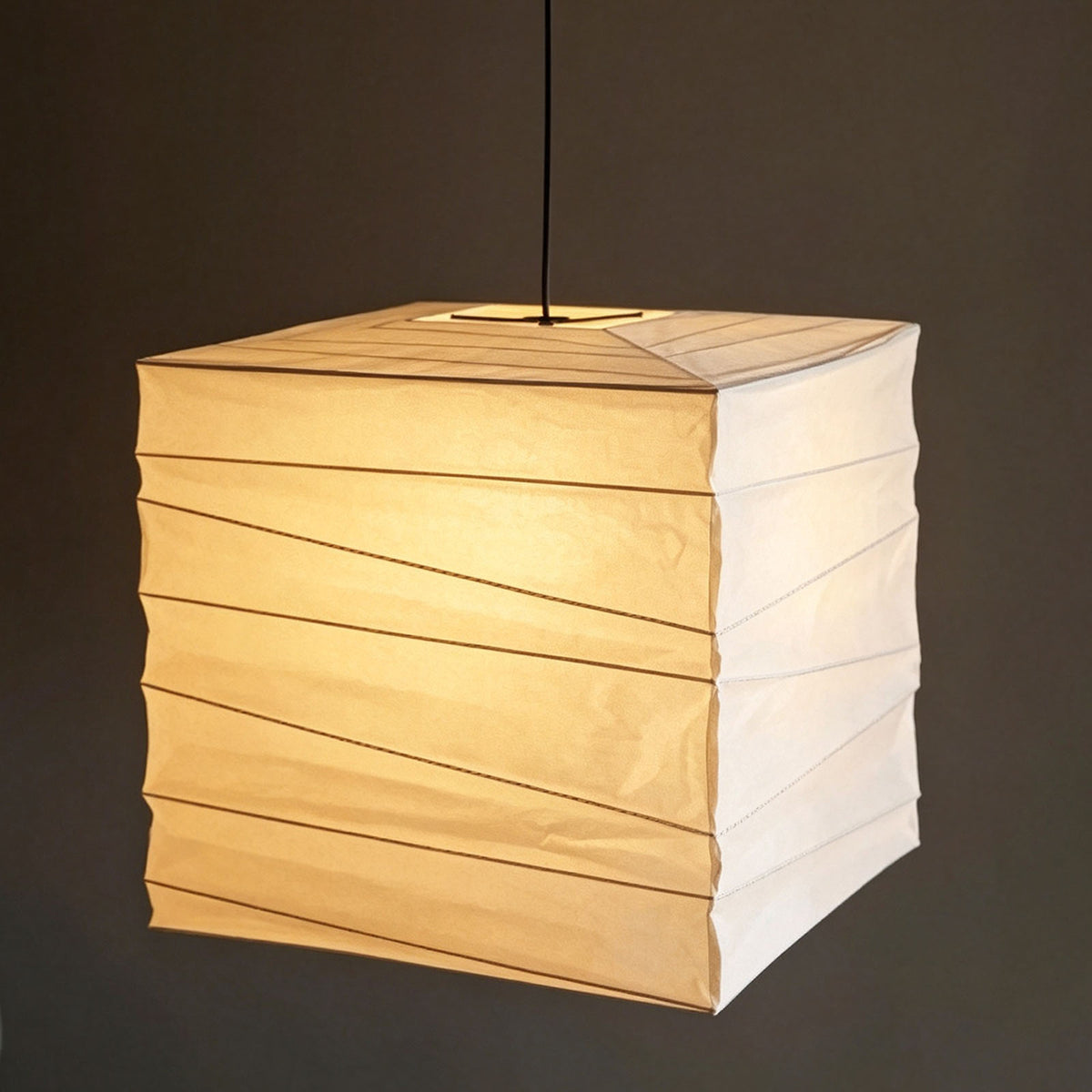 Marlen Squared Paper Column Pendant | Washi Paper and Metal | Hanging on a black cord glowing softly against a dark background | Severn Lighting