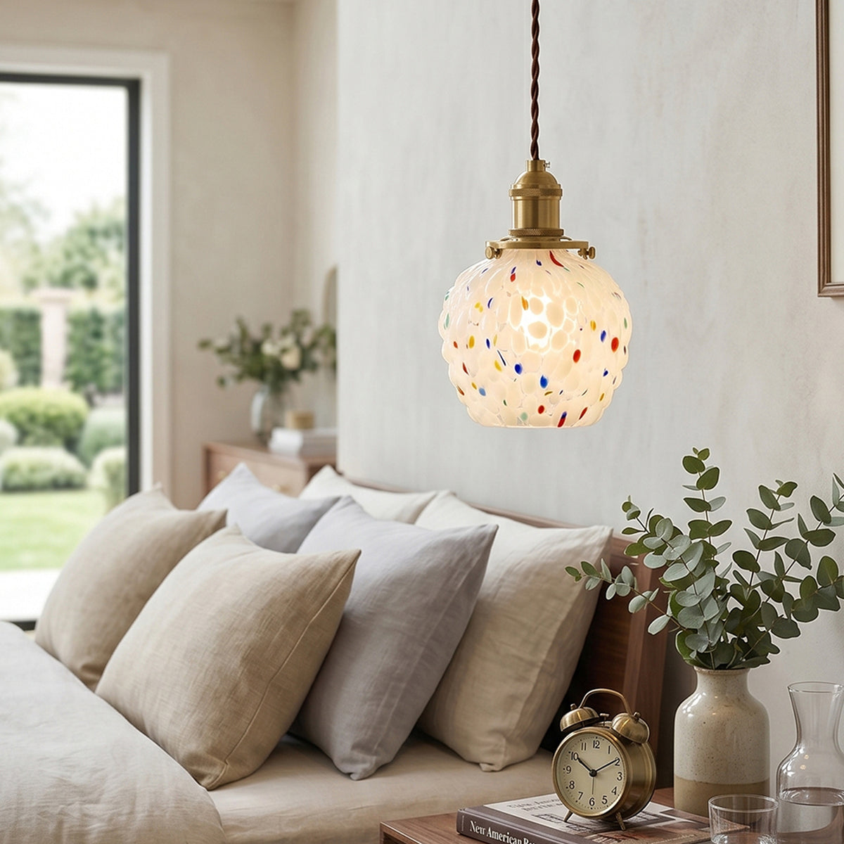 Marlowe Speckled Glass Pendant Lamp | Colorful Speckled Glass and Brass | Hanging above a bed with plush pillows and a beige headboard in a contemporary bedroom | Severn Lighting